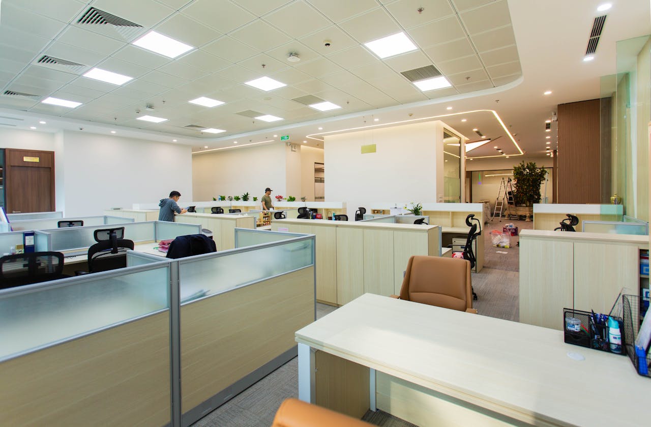 Bright and spacious office interior featuring open-plan cubicles, modern furniture, and ceiling lights.